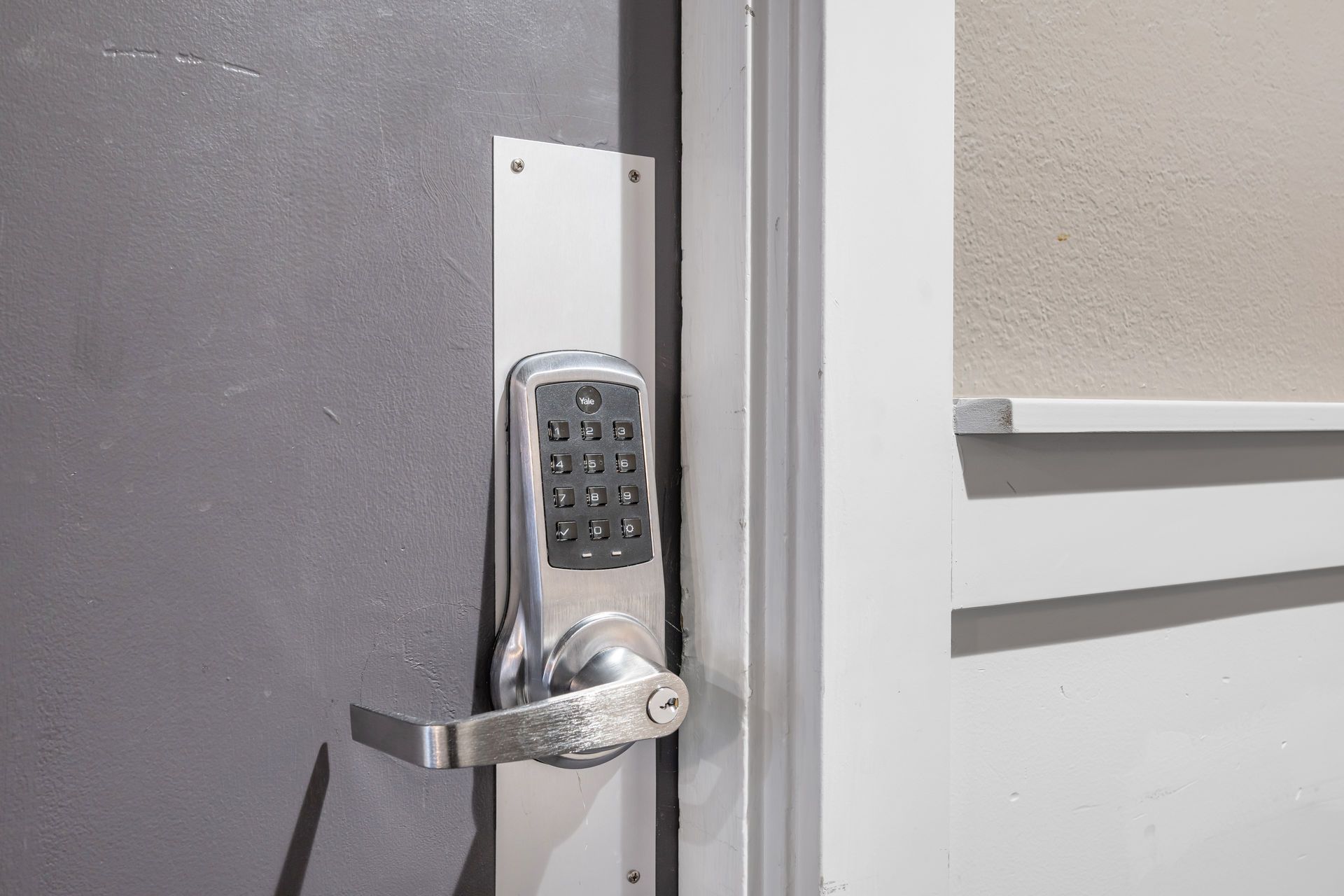 A silver keypad door lock on a gray door, next to a white door frame.