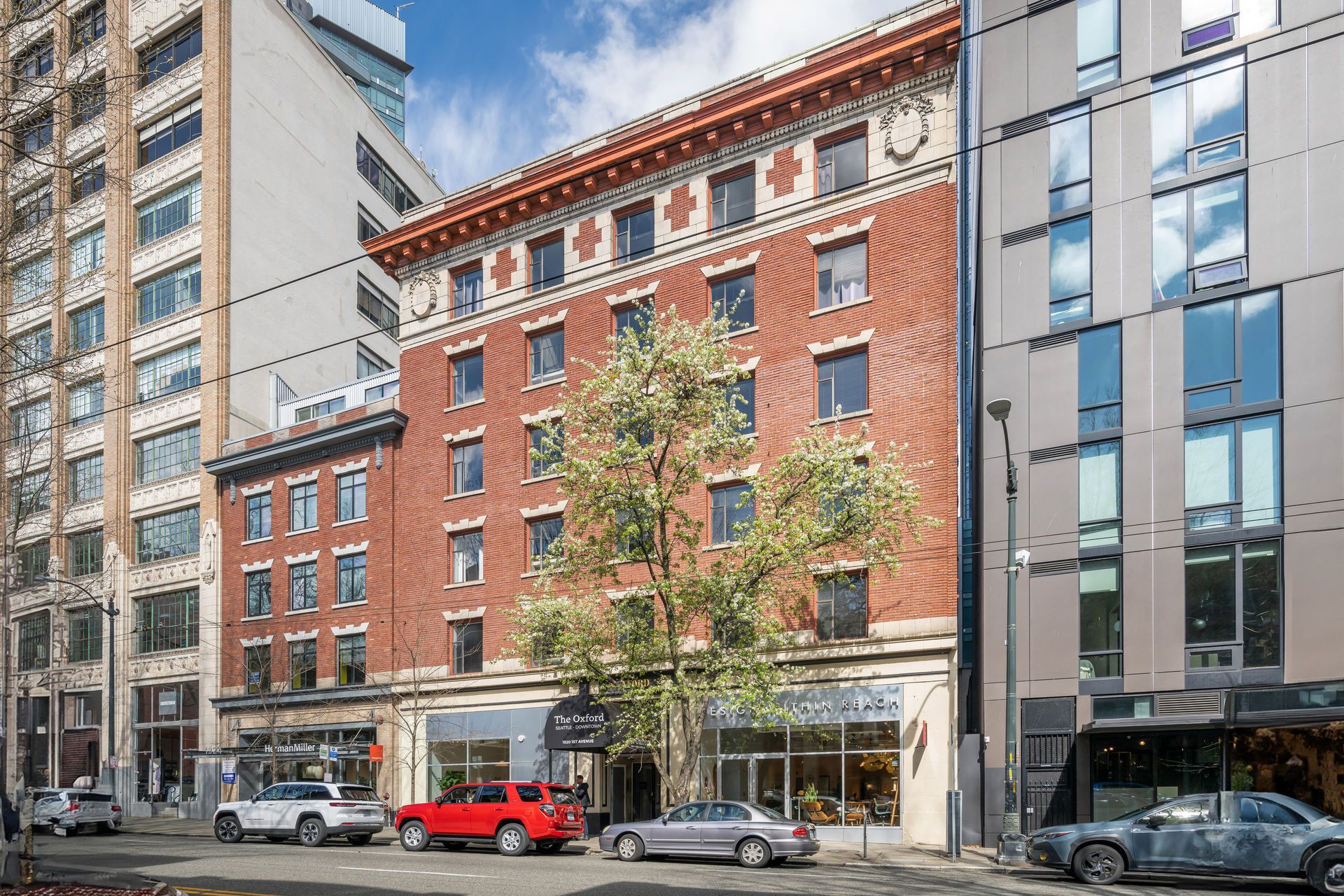 Brick building with ornate facade, trees in front, and cars parked on street.