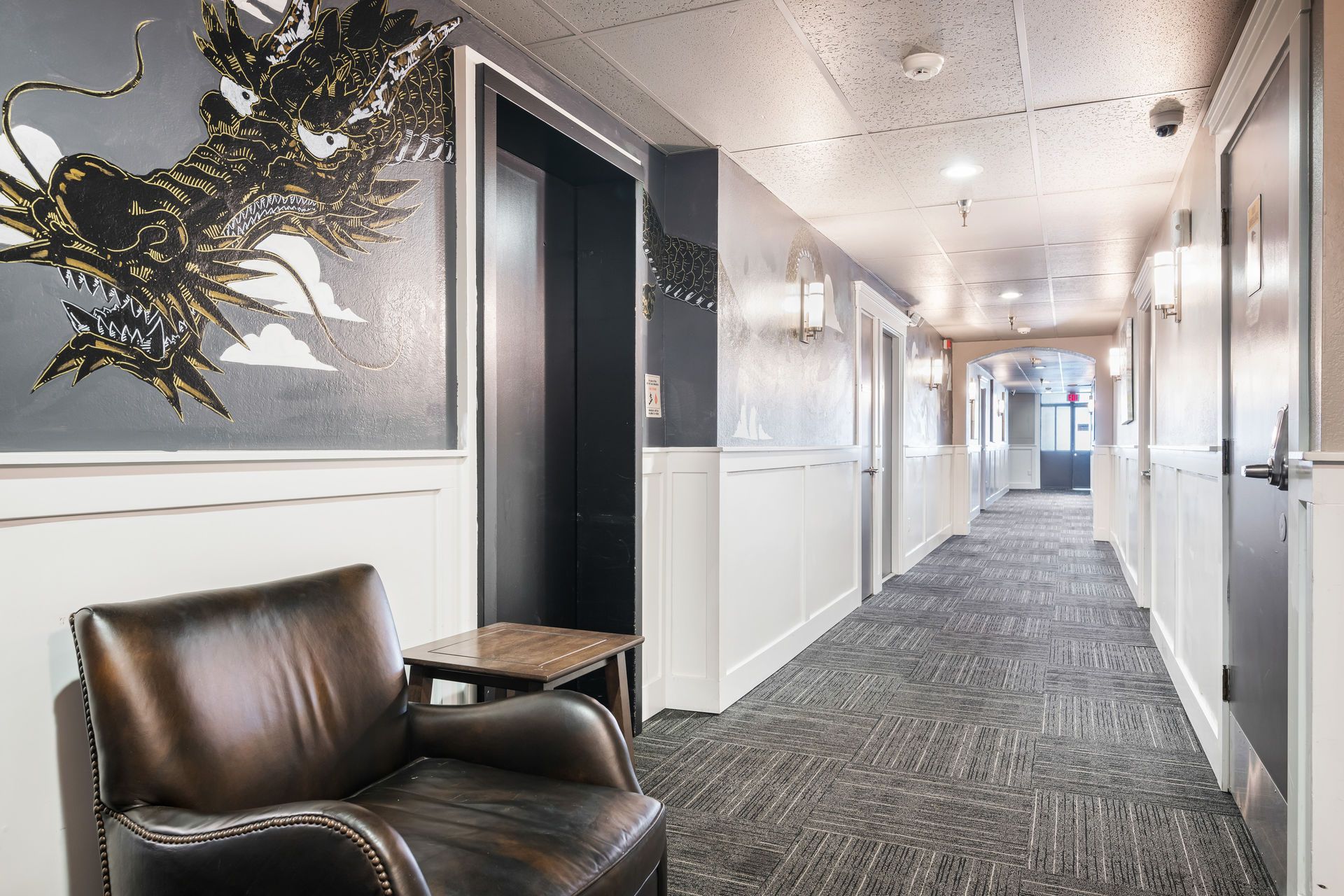 Hallway with chair, elevator, doors, and a decorative dragon art piece.