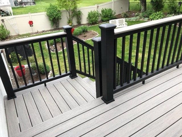 A deck with a black railing and stairs leading to a backyard.