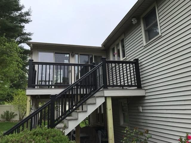 A white house with a black deck and stairs leading up to it.