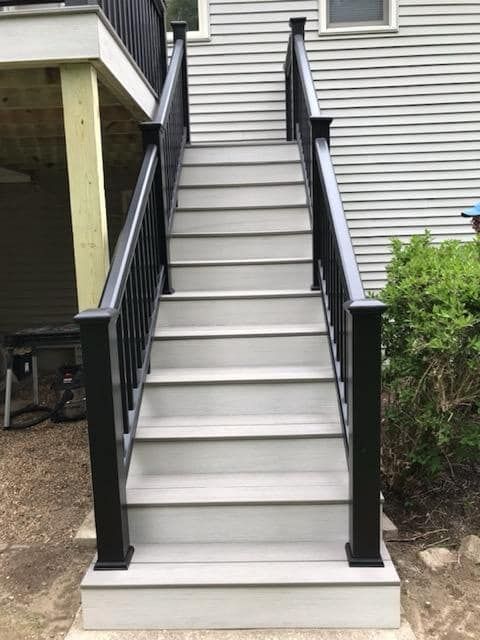 A set of stairs leading up to a deck with a black railing.