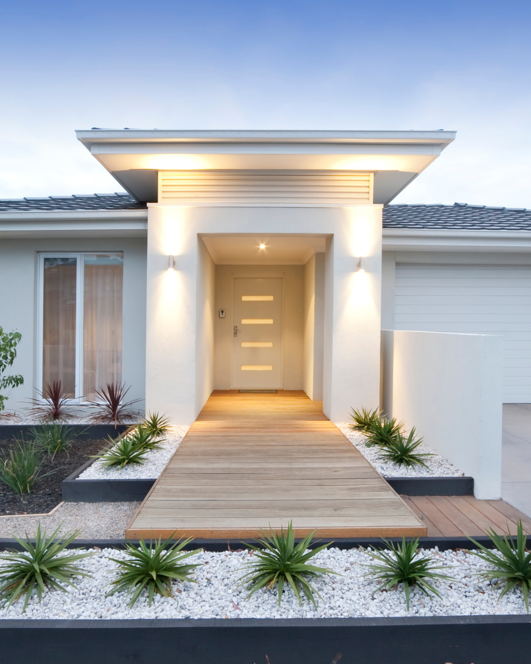 Modern home exterior with wooden walkway, white walls, and illuminated entrance.