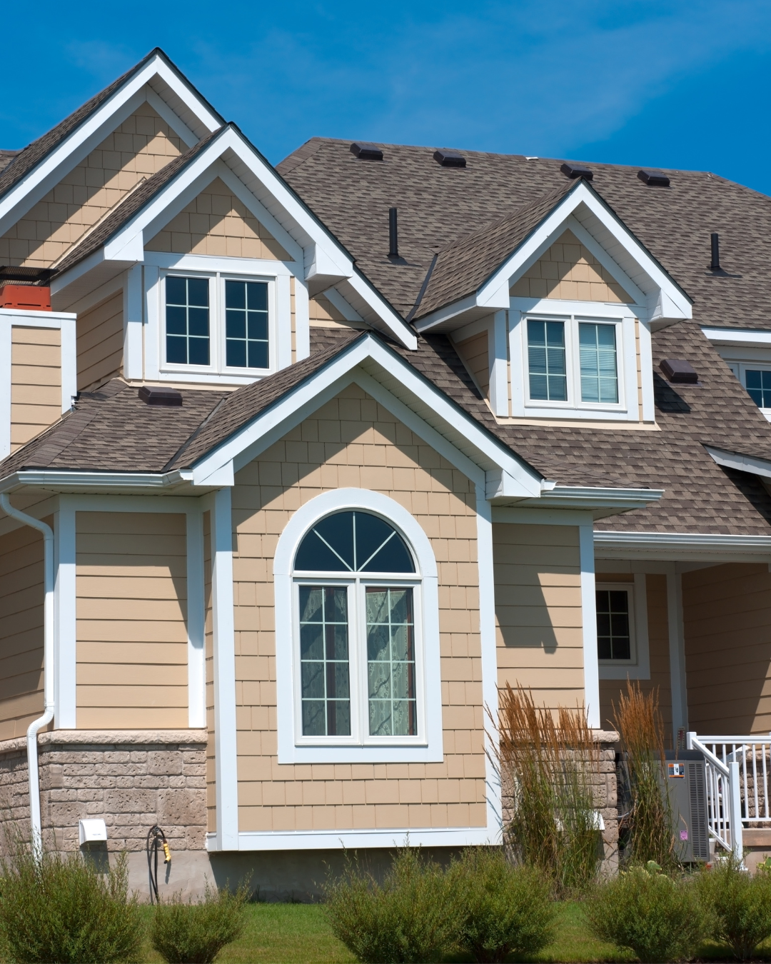 Tan house with white trim, arched window, and blue sky.