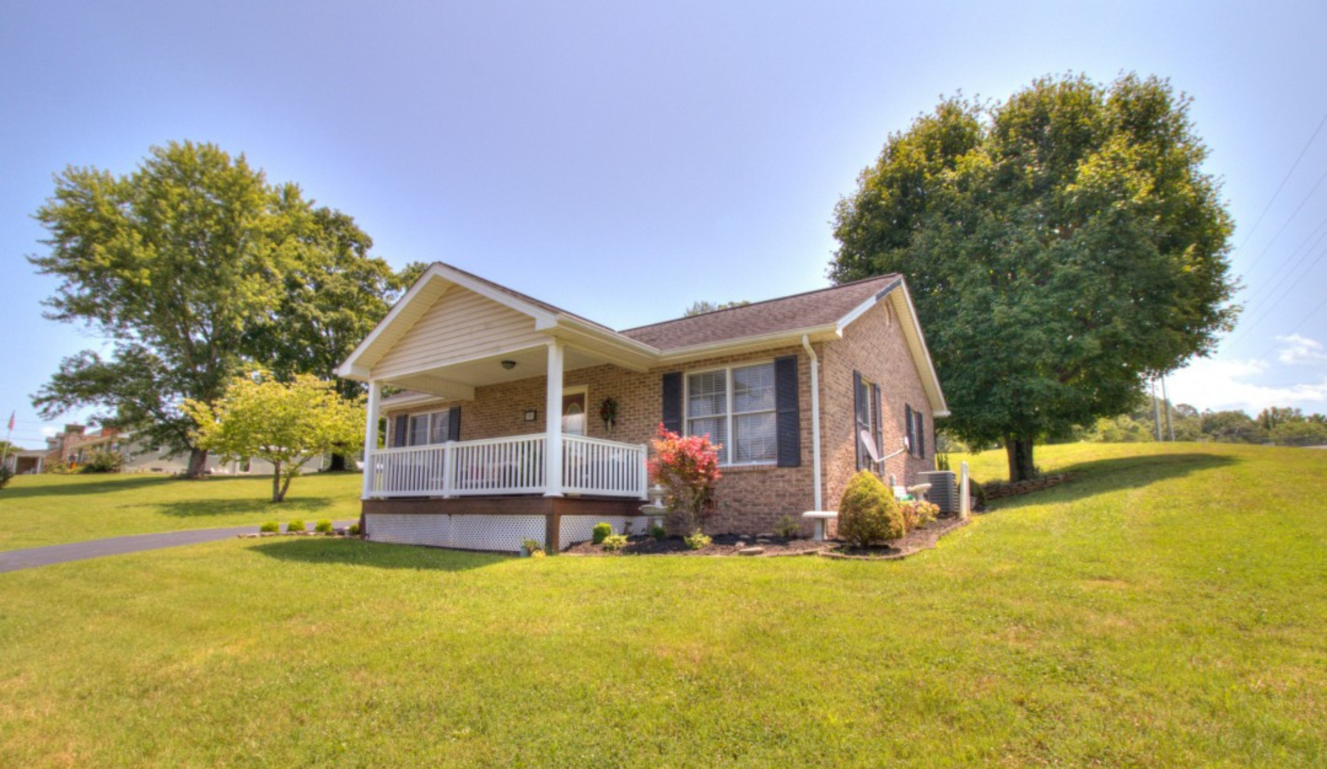 A small brick house with a porch is sitting on top of a lush green hillside.