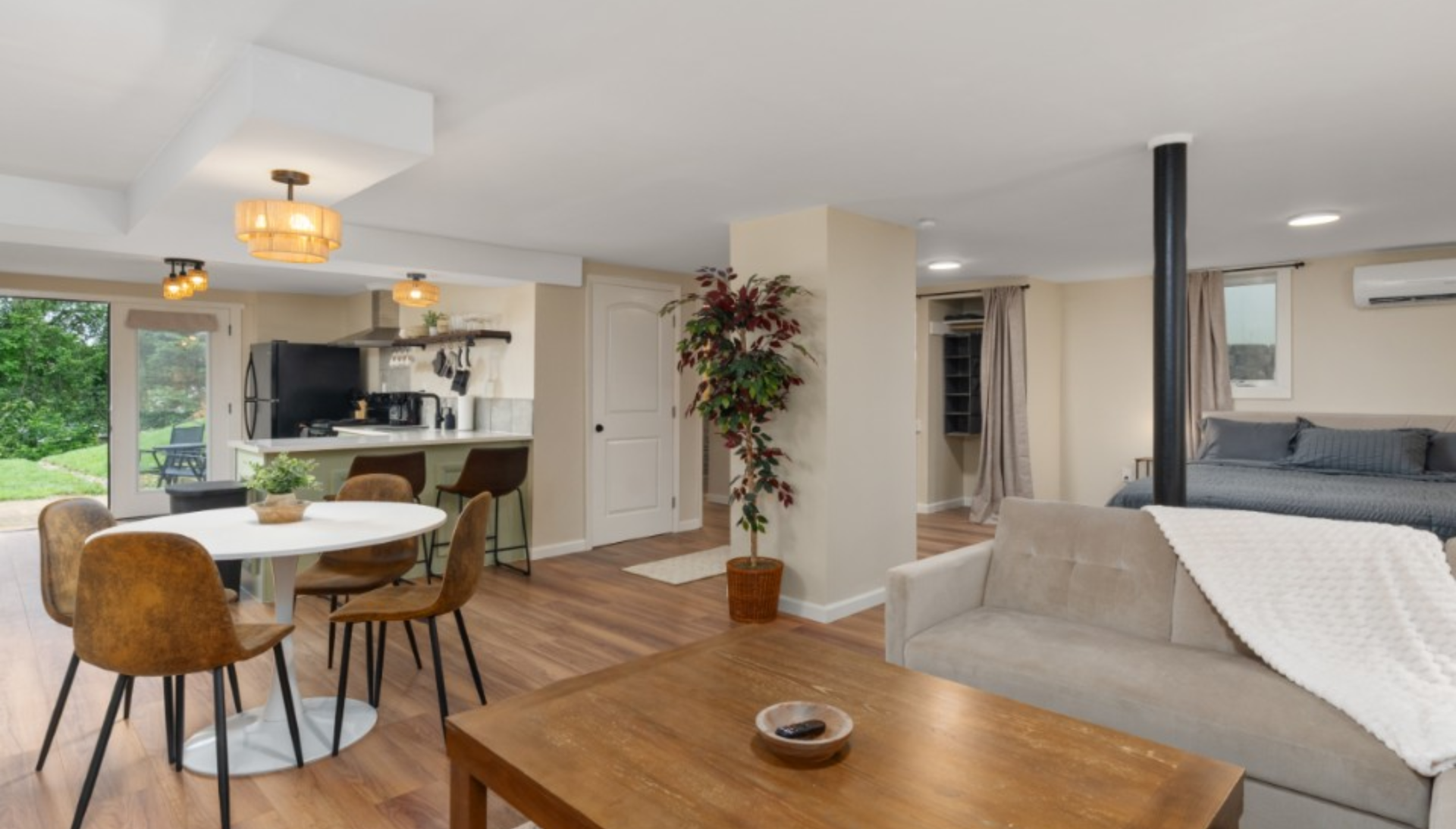 Book Now! Open concept living space: living room with sofa, dining area, and kitchen with wood floors, earth tones.