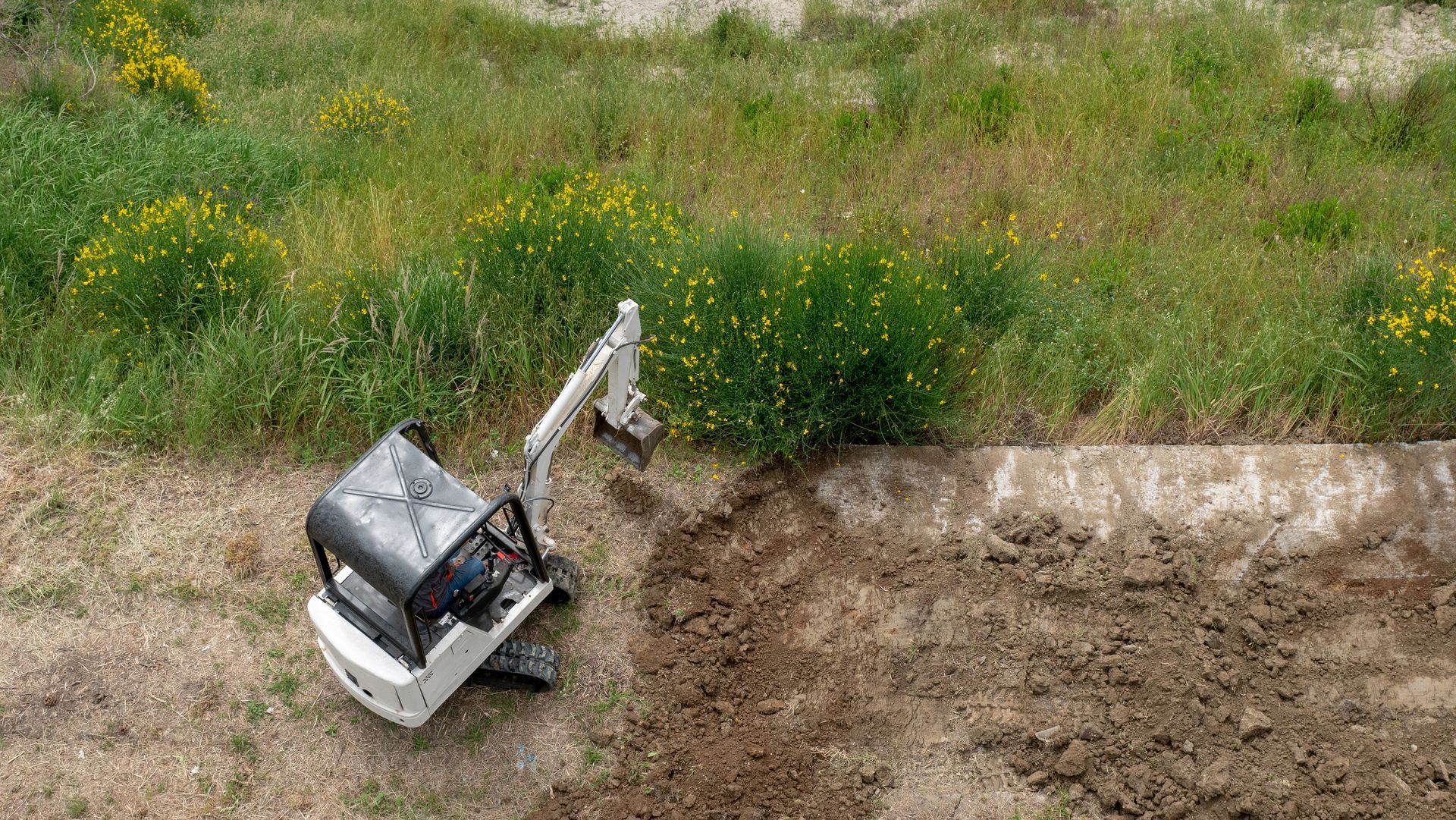 A small excavator is digging a hole in the dirt in a field.