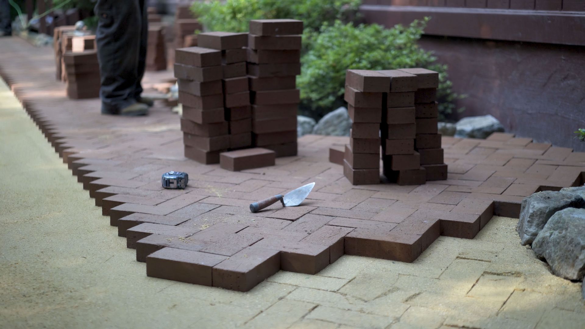 A man is laying bricks on a sidewalk.