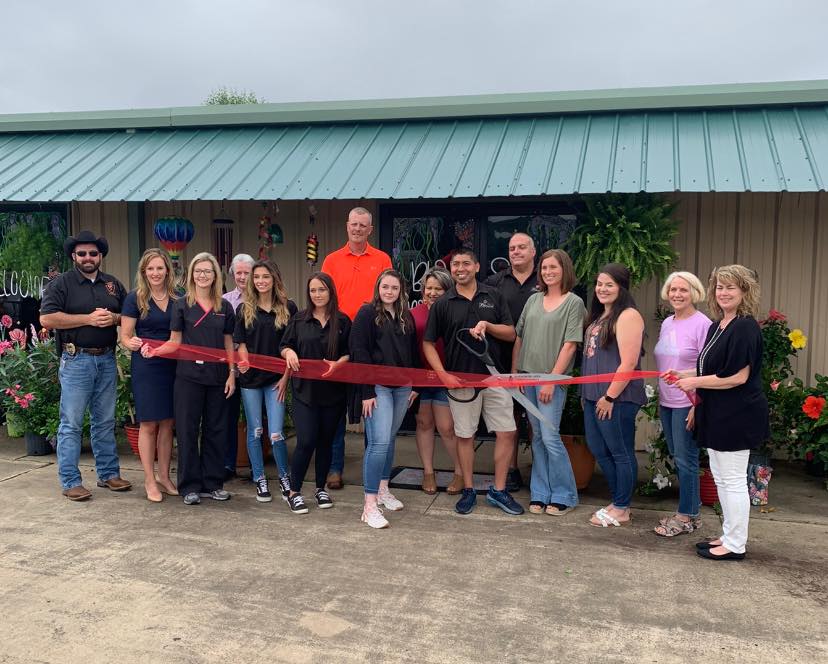 A group of people are standing in front of a building holding a red ribbon.