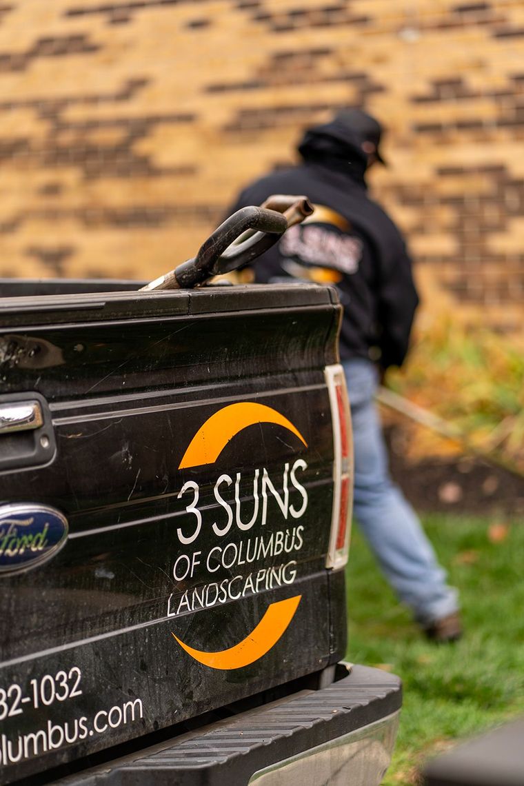 Black truck bed with landscaping company logo, 3 Suns of Columbus. Man working in background.