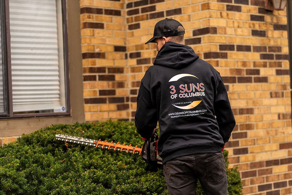 Man trimming a bush with hedge trimmers, wearing a black hoodie with 
