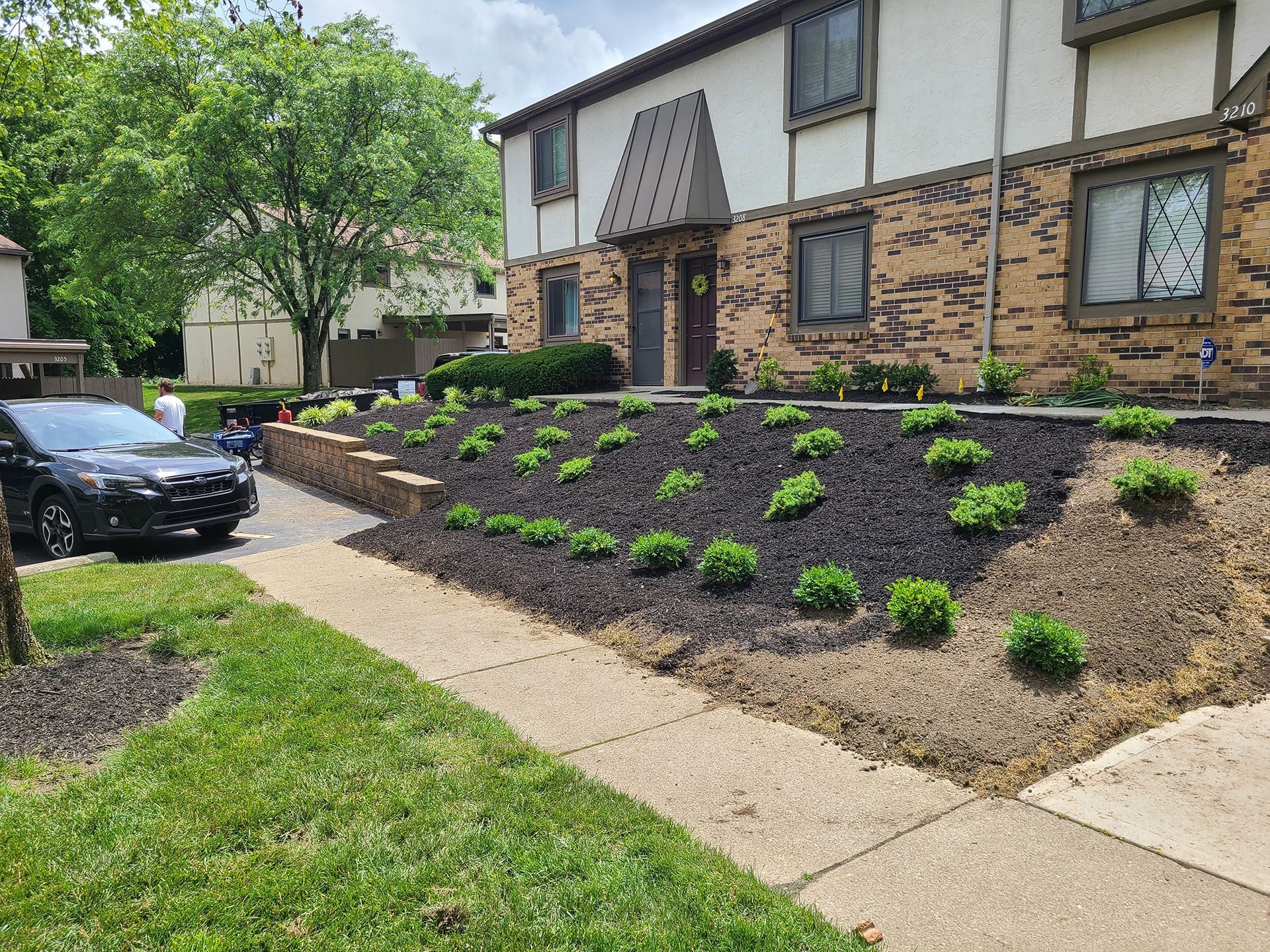 Black car parked near a landscaped apartment building with freshly mulched flowerbeds and shrubs.