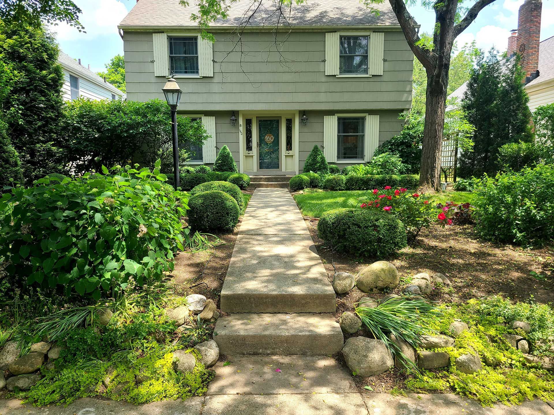 Two-story green house with a stone walkway and well-manicured landscaping.