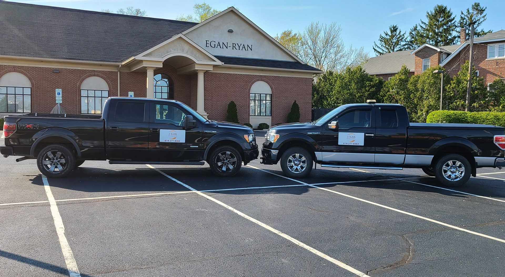 Two black pickup trucks parked in front of a brick building with a sign that reads 