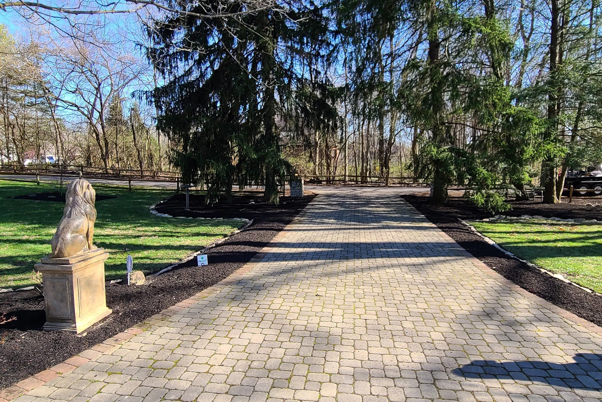 Brick driveway lined with dark mulch, trees, and a stone lion statue.