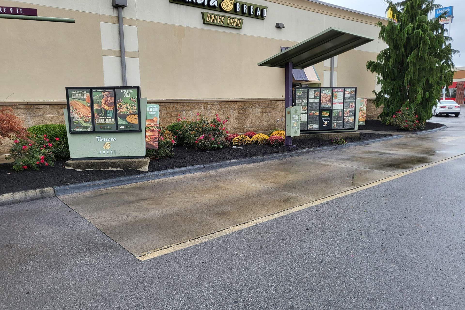 Drive-thru lane at a restaurant with a menu and flower bed.