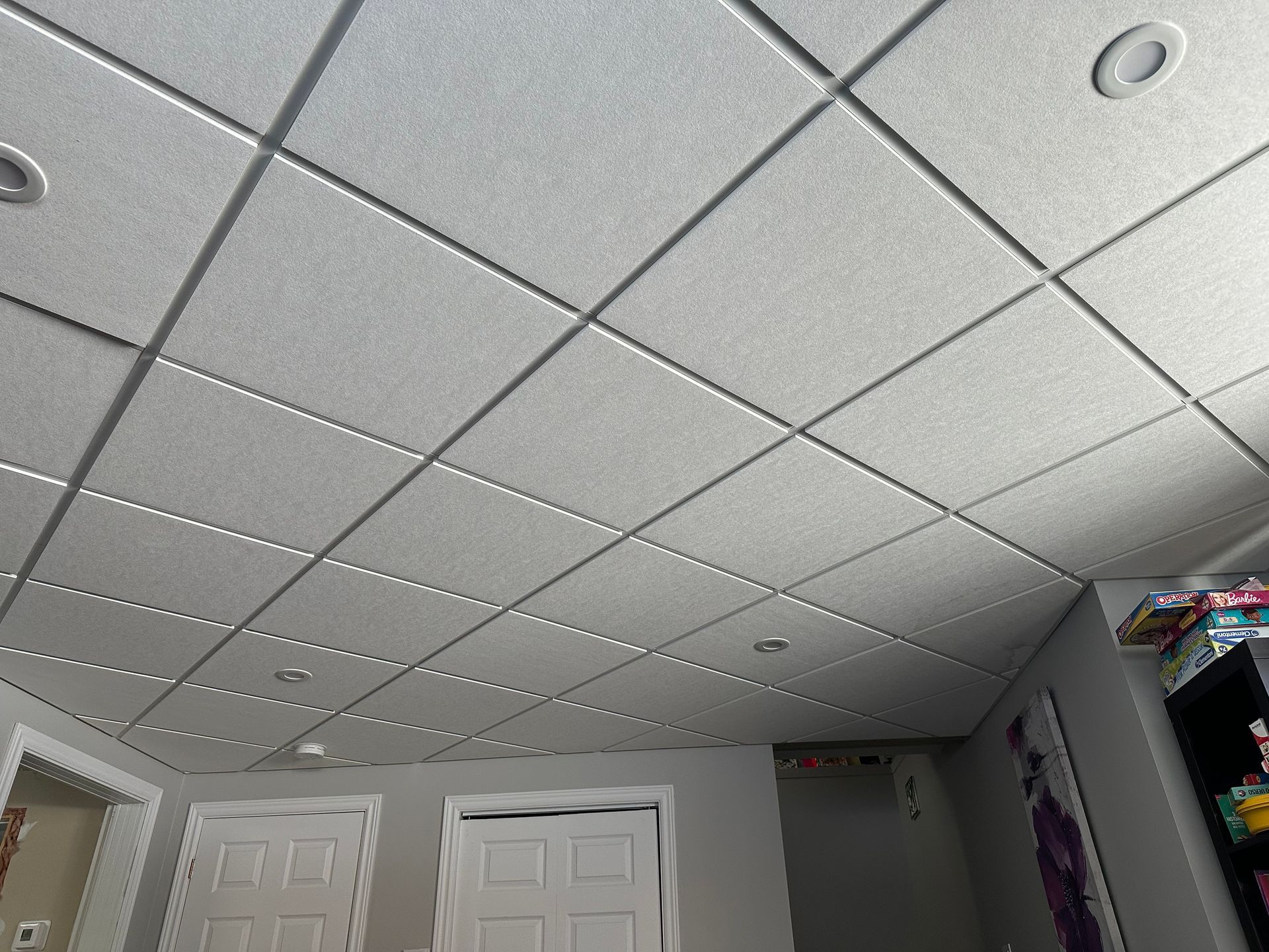 Un faux plafond composé de panneaux carrés blancs et d'un éclairage encastré intégré dans une pièce aux murs gris et comportant deux portes.