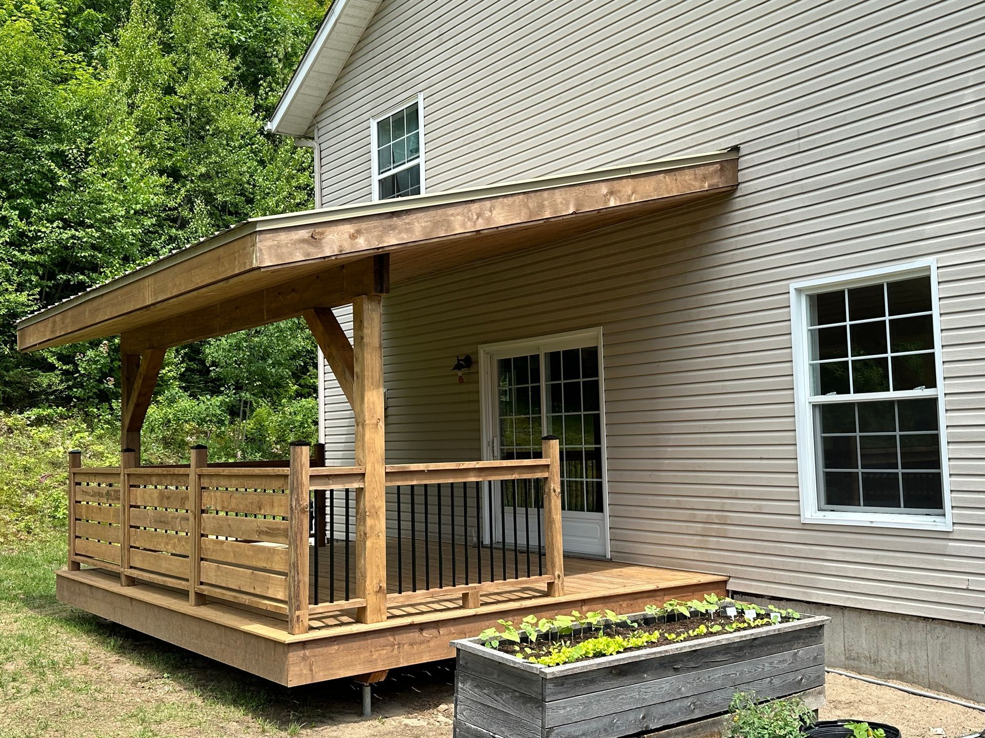 Une terrasse en bois avec un toit couvert, des rambardes et une jardinière rectangulaire devant une maison au revêtement extérieur en vinyle de couleur claire.