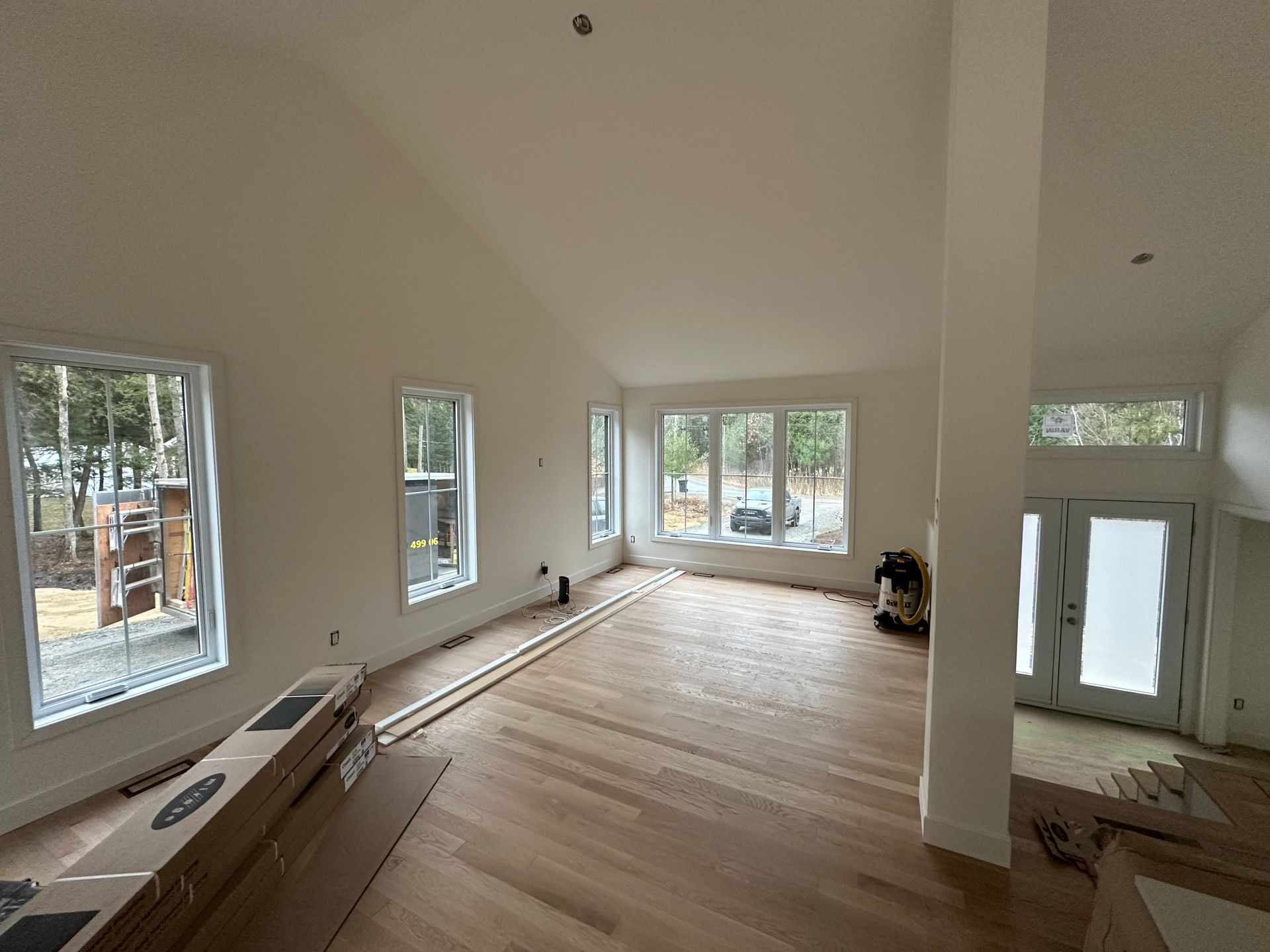 Un salon lumineux, encore inachevé, avec parquet, plafonds blancs voûtés et grandes fenêtres donnant sur l'extérieur.