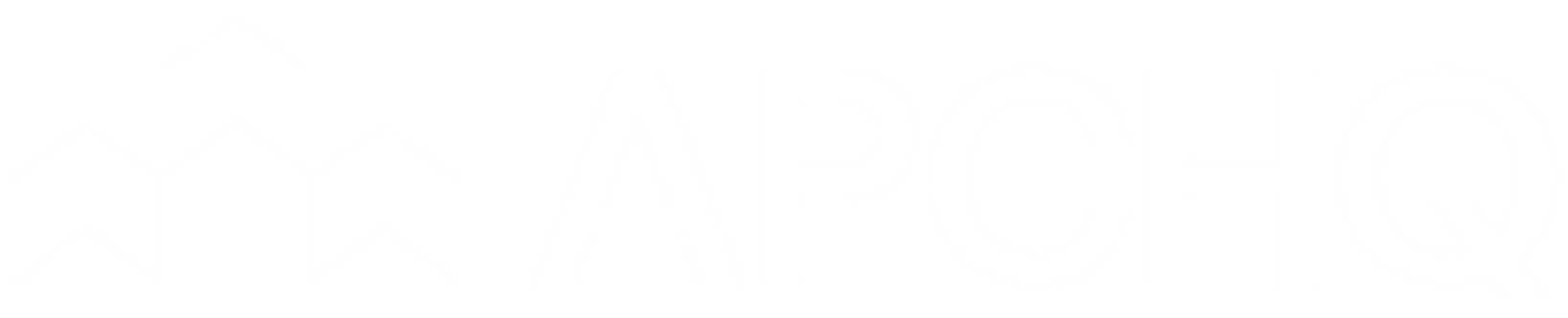 Un petit chien à la robe claire se tient debout sur une surface blanche, portant un harnais bleu et un bandana à motifs colorés.