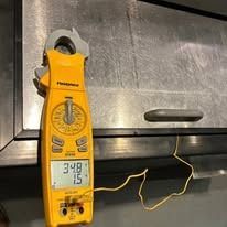 A yellow clamp meter is hanging on a stainless steel cabinet.