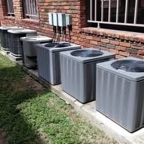 A row of air conditioners are sitting on the side of a brick building.