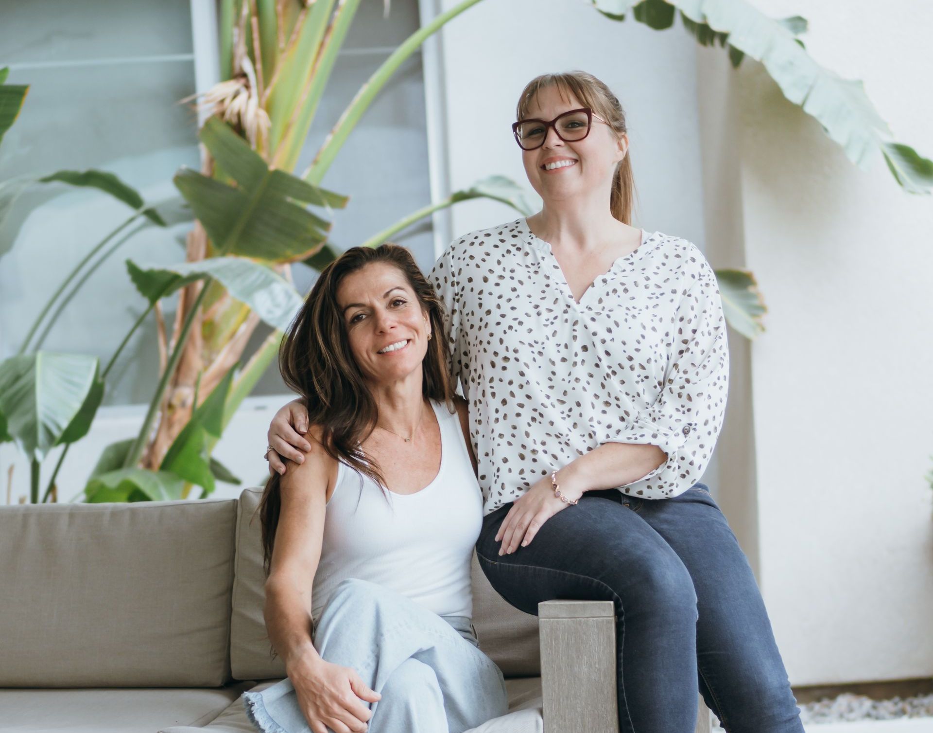 Two women are posing for a picture while sitting on a couch.