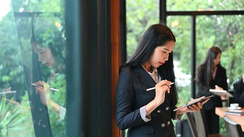 Asian business woman near a long window and looking at a tablet.