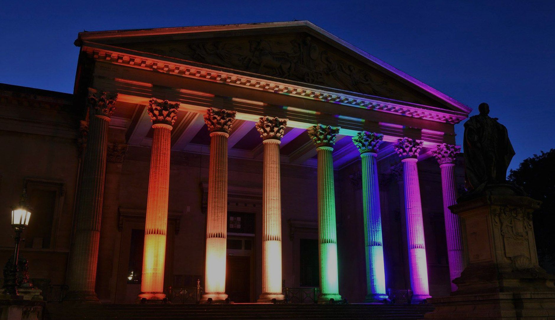 Colonade and pillars of a University of Bristol building lit up colourfully at night