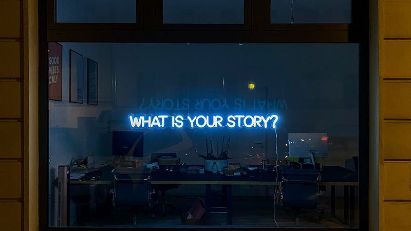 Window with a neon sign reading: What's Your Story?