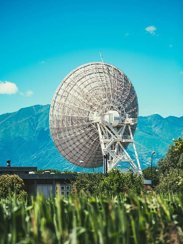 A large satellite dish in a pristine landscape with grass in foreground and blue mountains behind