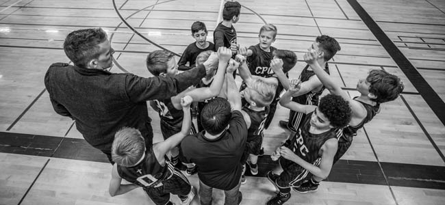 B&W image of coach and kids in basketball team joining hands