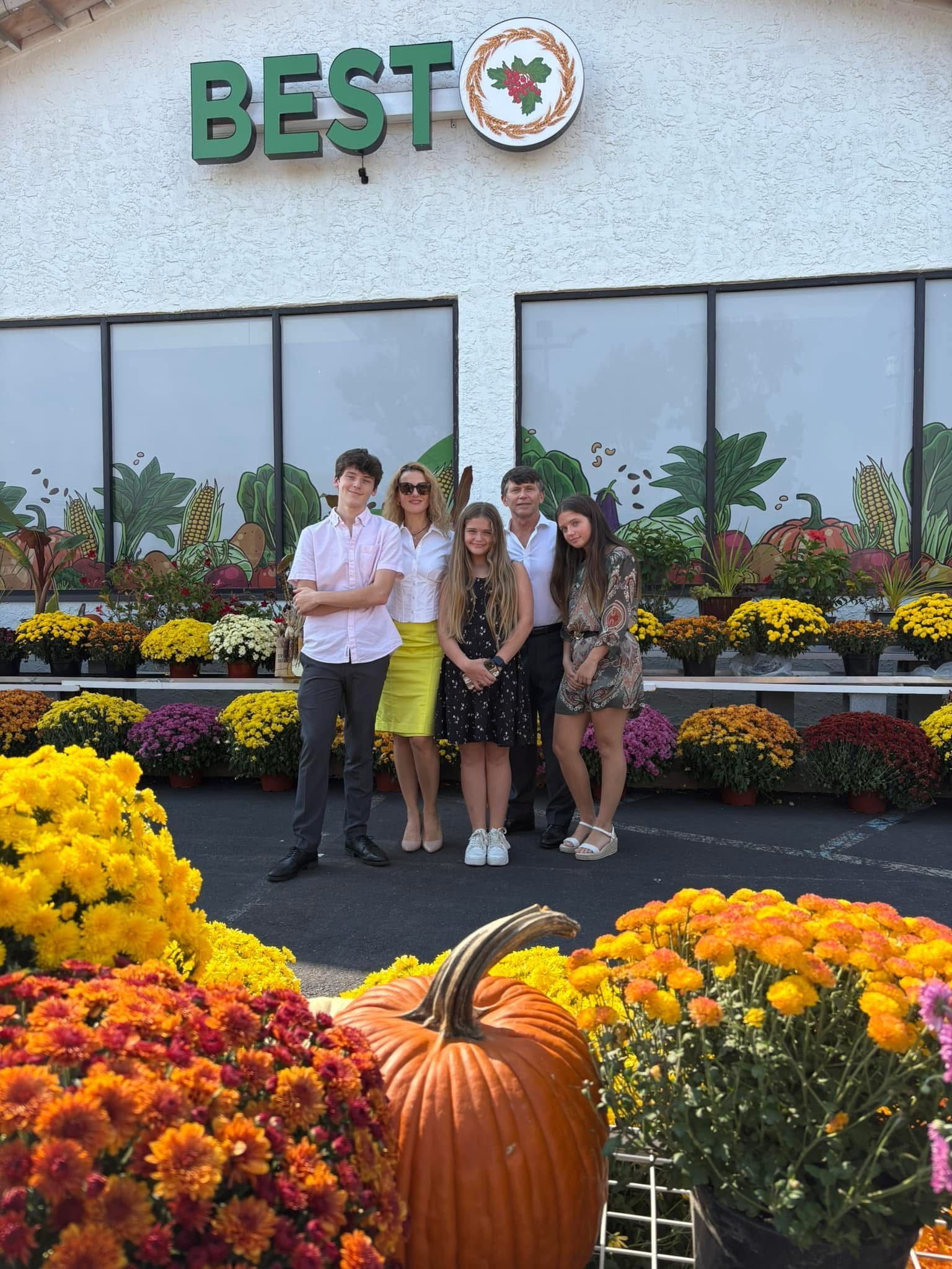 A group of people are standing in front of a store surrounded by pumpkins and flowers.