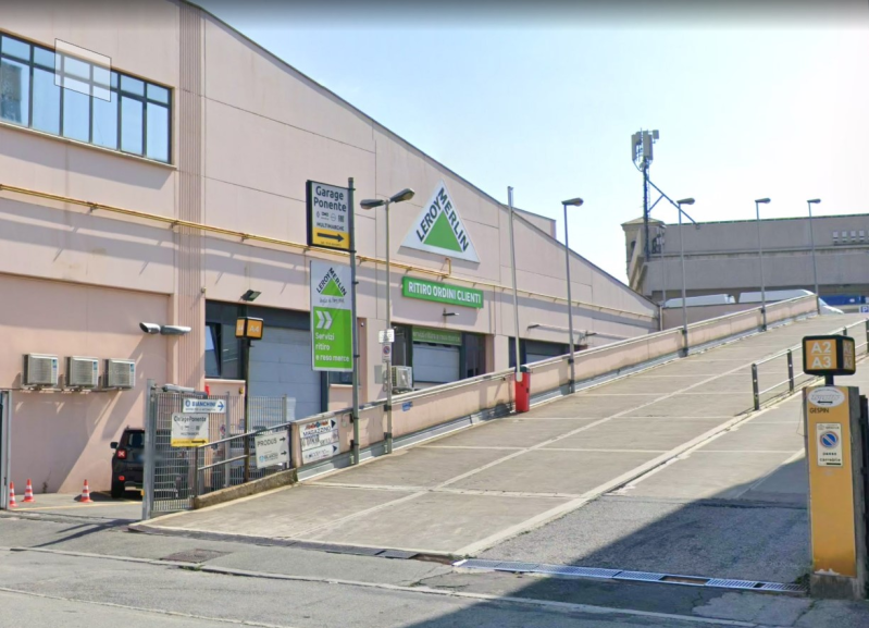 Un'ampia rampa di cemento conduce a un grande edificio rosa con insegne verdi e un ingresso con cancello.