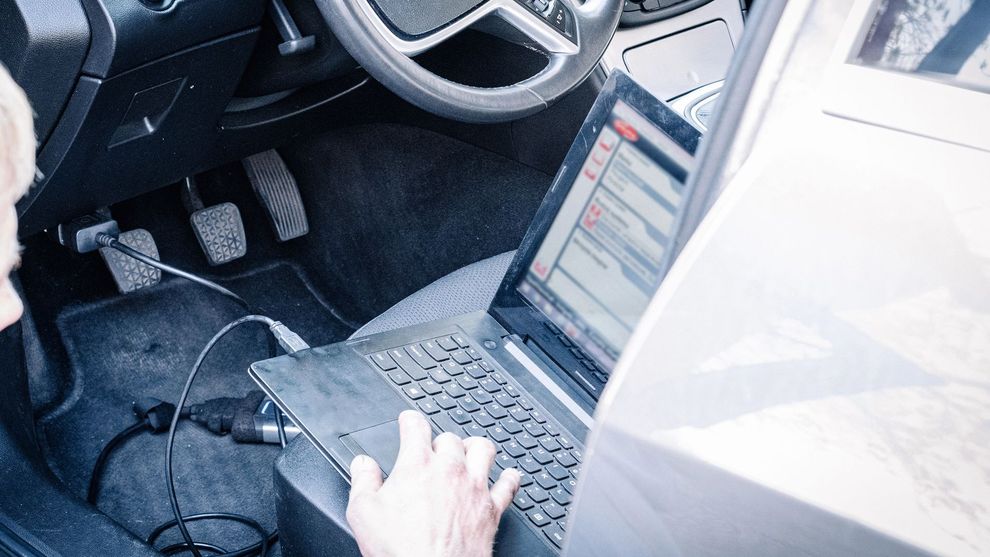 Una persona utilizza un computer portatile collegato tramite cavo alla porta diagnostica di un veicolo per eseguire un'ispezione o una riparazione dell'auto.