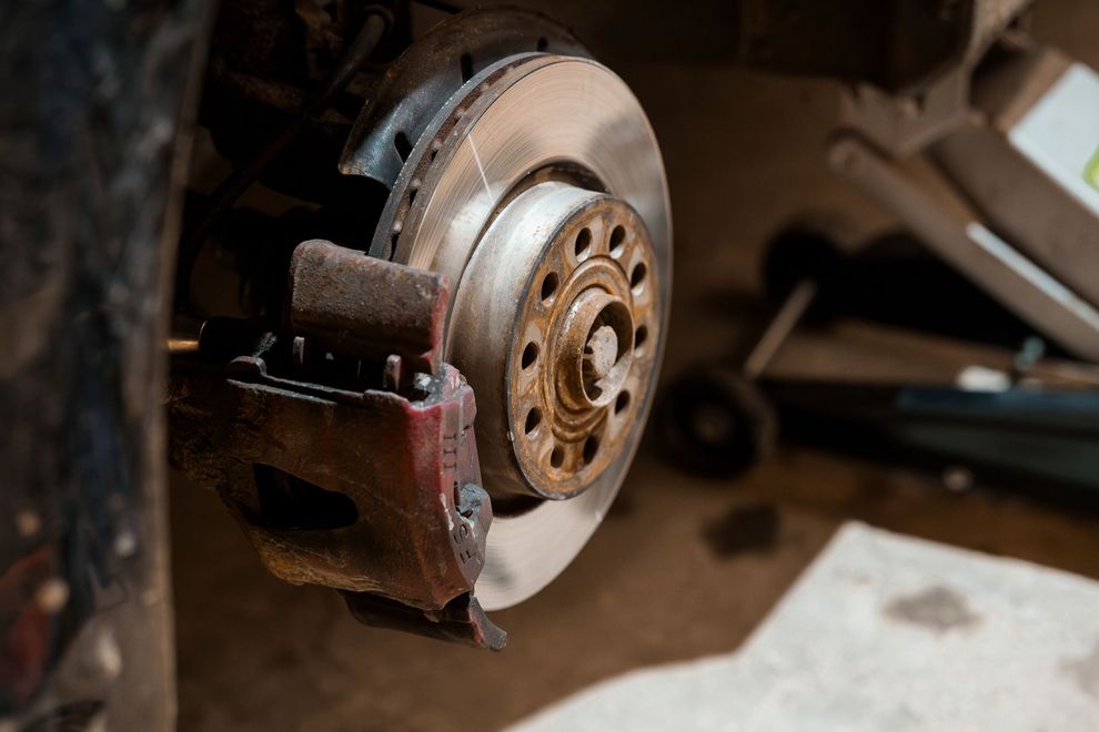Durante la manutenzione, si vedono il disco freno e la pinza freno rossa di un'auto, con un cric idraulico sullo sfondo.