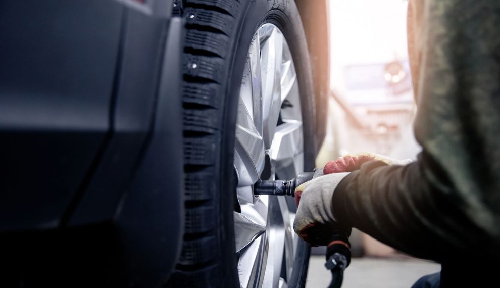 Primo piano di un meccanico con i guanti da lavoro che usa una chiave a percussione per serrare i dadi di fissaggio di uno pneumatico di un'auto.