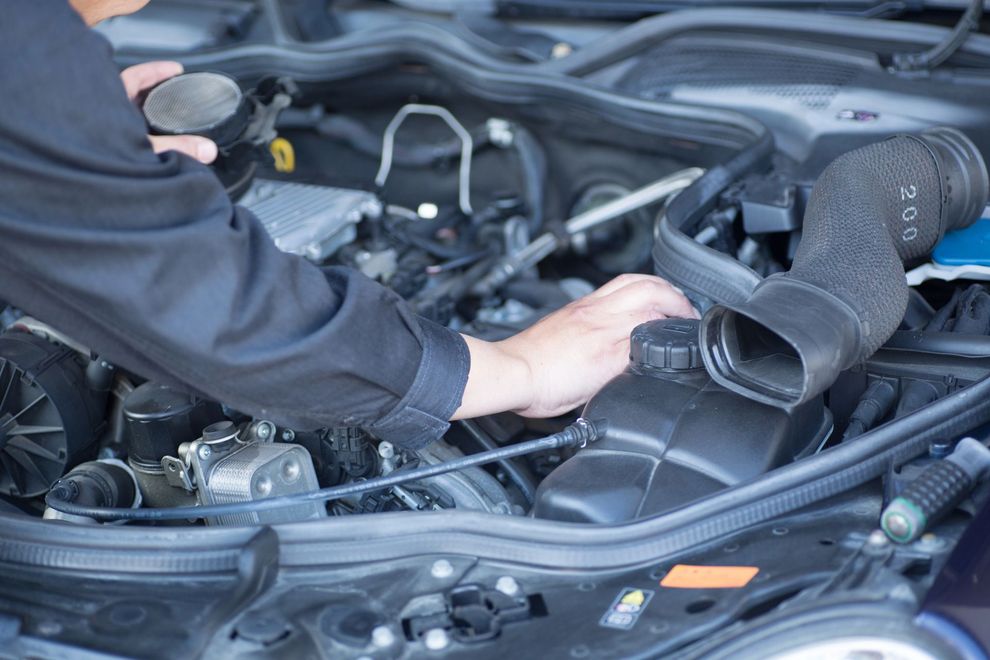 Un meccanico in uniforme nera esegue interventi di manutenzione sotto il cofano di un motore.