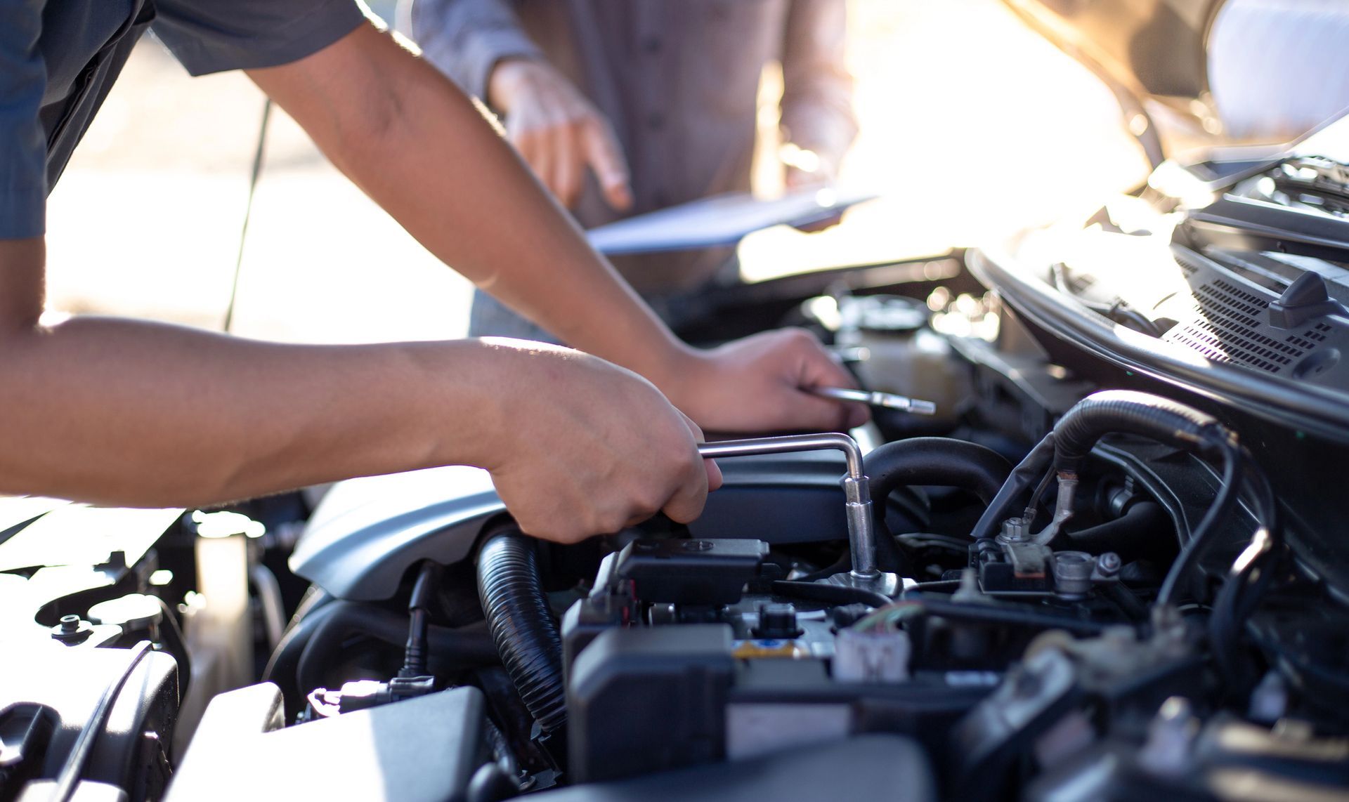 Un meccanico utilizza una chiave a cricchetto per lavorare sul motore di un'auto, mentre un assistente tiene un blocco appunti nelle vicinanze.