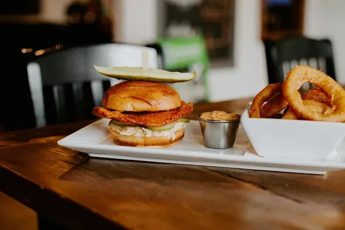 Cocktail in a globe glass with fruit slices and a mini bottle of tonic water on a wooden surface.
