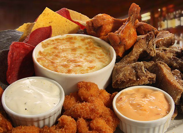 Appetizer platter: chips, cheese dip, wings, fried shrimp, and dipping sauces.