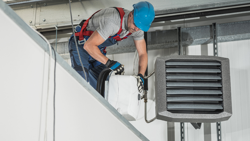 Worker in blue hard hat installing equipment on an industrial rooftop near a large vent.