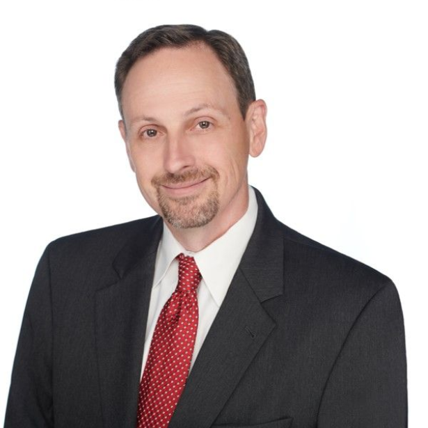 Man in suit and tie smiles, facing slightly to the left.