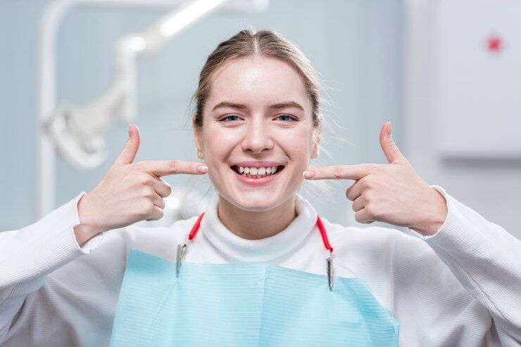 A woman is pointing at her teeth in a dental office.