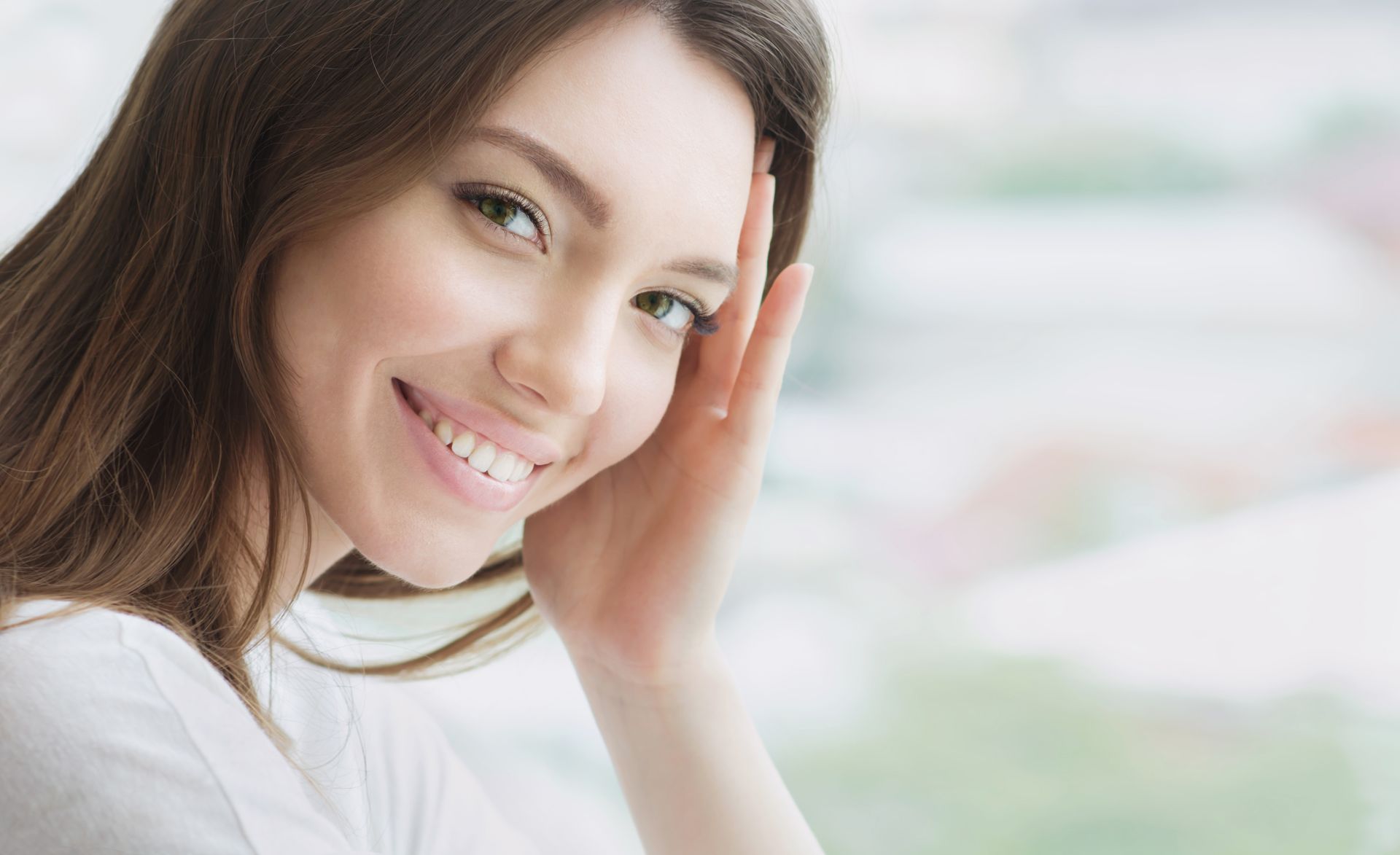 A woman is smiling and touching her face with her hand.