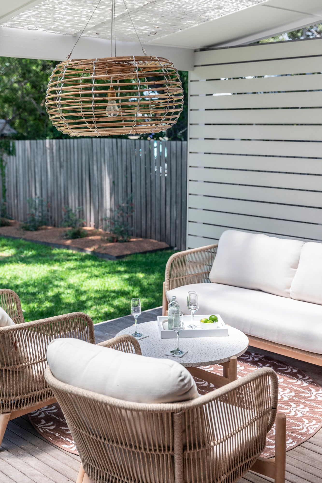 An inviting outdoor lounge area with a wooden sofa set, complete with soft pillows, emanates a sense of comfort and style in this interior design.— Caroline Jolly Interiors in Wollongong, NSW