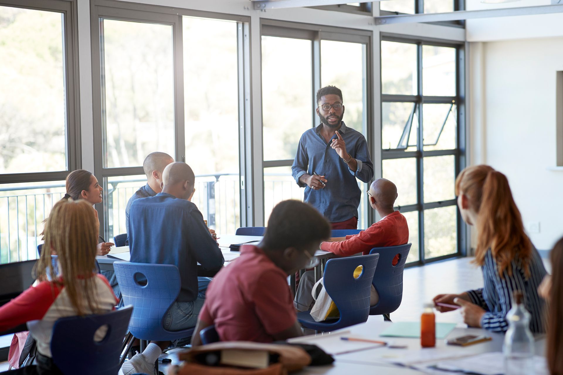 Teacher in blue shirt leads discussion with students in a classroom.