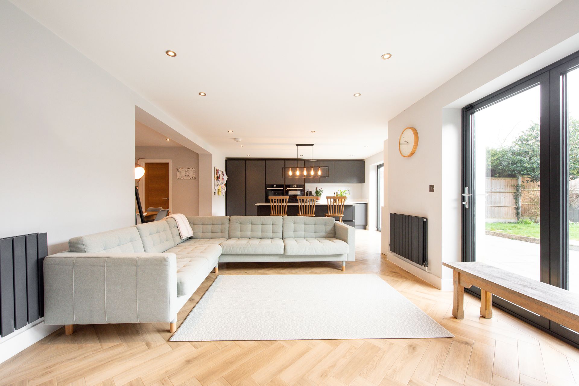 Open-plan living space with a gray sectional sofa, modern kitchen, and large glass doors to the backyard.
