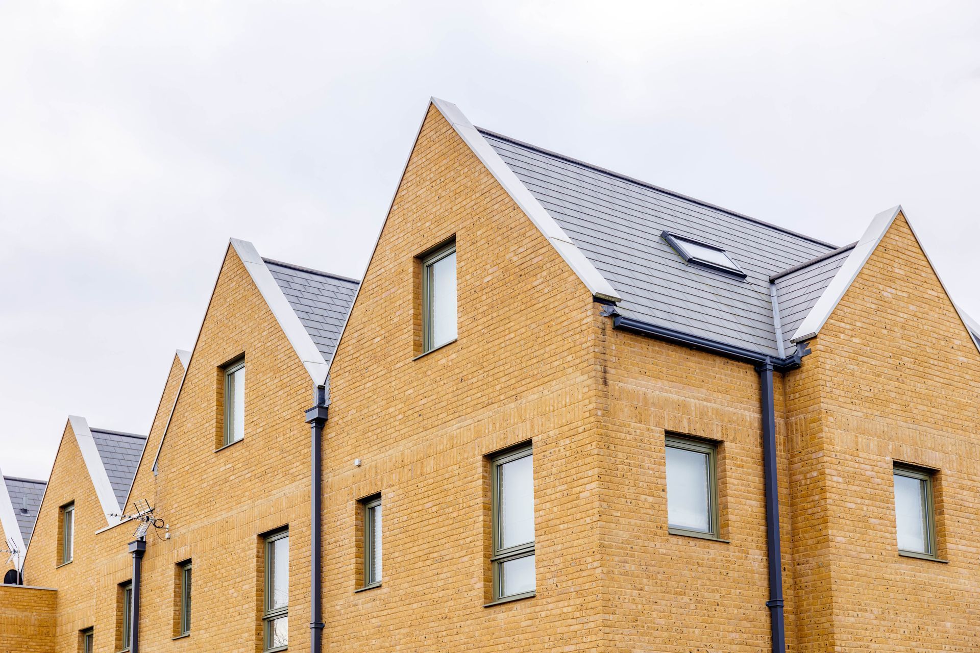 Yellow brick buildings with gray gabled roofs and windows against a cloudy sky.