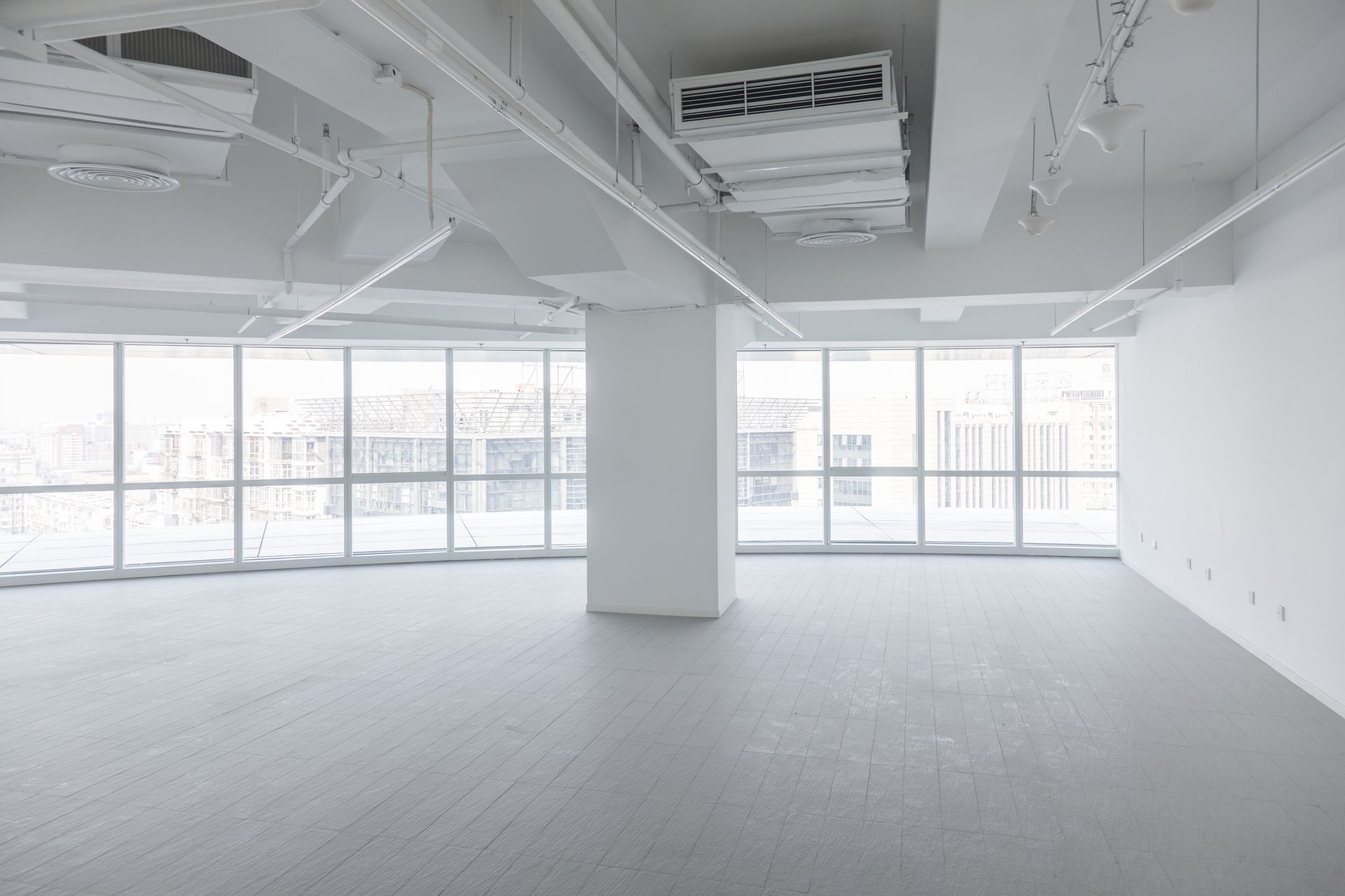 Empty, bright white office space with large windows and exposed ceiling fixtures.